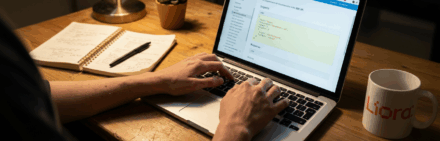 Développeur tapant du code pour une API sur un ordinateur portable, avec un carnet de notes et une tasse sur le bureau.