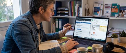 Femme travaillant sur son ordinateur portable à un bureau, prenant des notes avec des tasses de café à proximité.