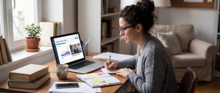 Femme assise à un bureau, prenant des notes devant un ordinateur portable, entourée de livres et de fournitures d'étude, illustrant l'apprentissage à temps partiel.