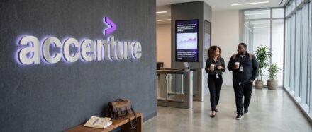 Dos profesionales caminando por el interior de la oficina de Accenture, con el logotipo de Accenture expuesto de forma destacada en la pared.