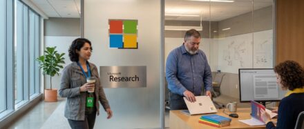 Una escena de oficina que muestra a dos empleados interactuando en un espacio de investigación con el logotipo de Microsoft de fondo.