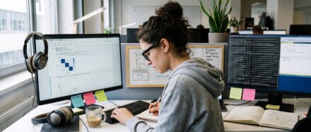 A data scientist working on charts and data across multiple computer screens in a modern office.