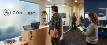 Two employees interacting in the Confluent office, showcasing a modern workspace and logo, highlighting the innovative atmosphere related to Kafka features.